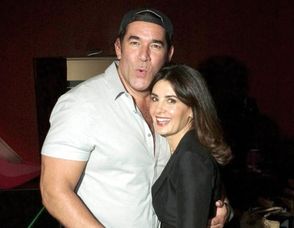 Eduardo Santamarina poartă un tricou alb și o șapcă și o ține pe Mayrin Villanueva în brațe