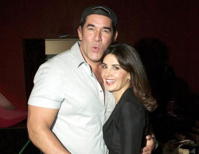 Eduardo Santamarina poartă un tricou alb și o șapcă și o ține pe Mayrin Villanueva în brațe