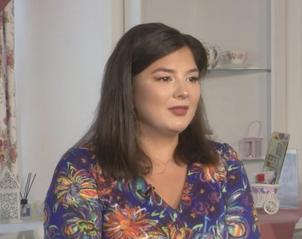 Maria Popovici poartă o rochie cu flori, cu mâneci lungi și are părul scurt. Artista îl poartă desprins și are un machiaj simplu