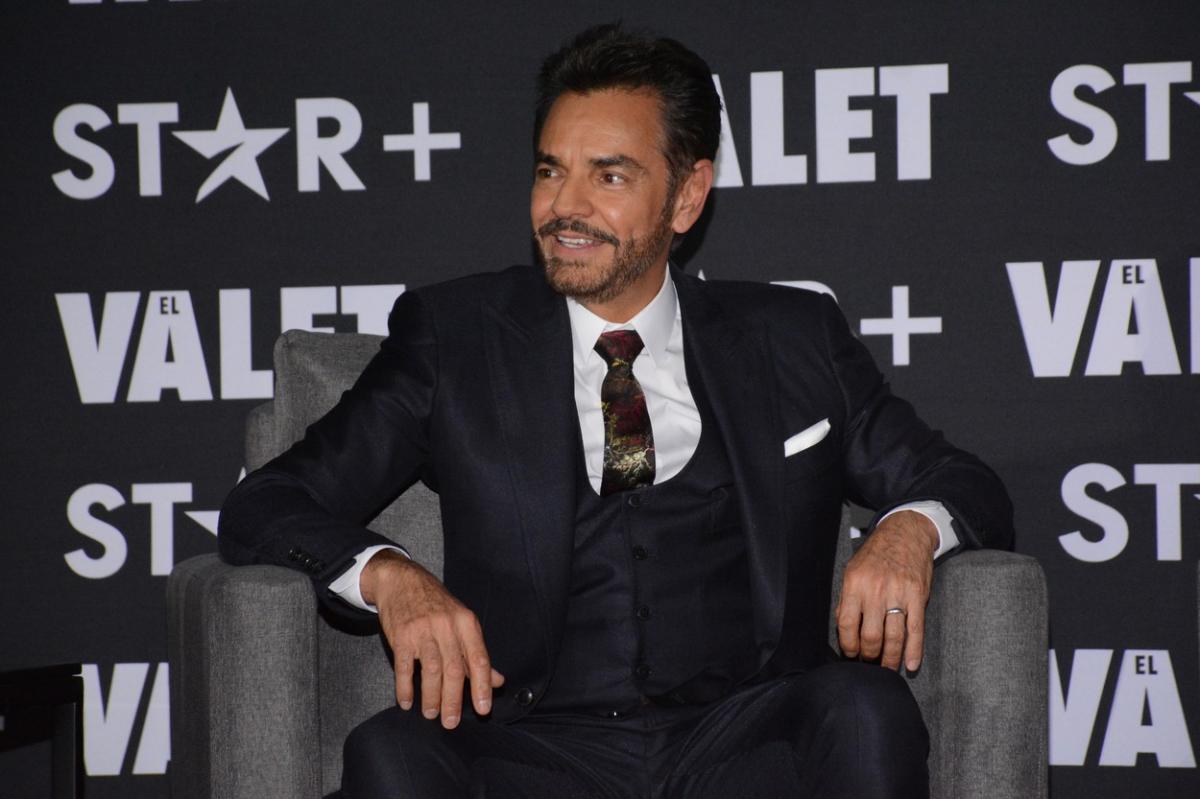 Eugenio Derbez poartă un costum negru și cămașă albă. Actorul zâmbește