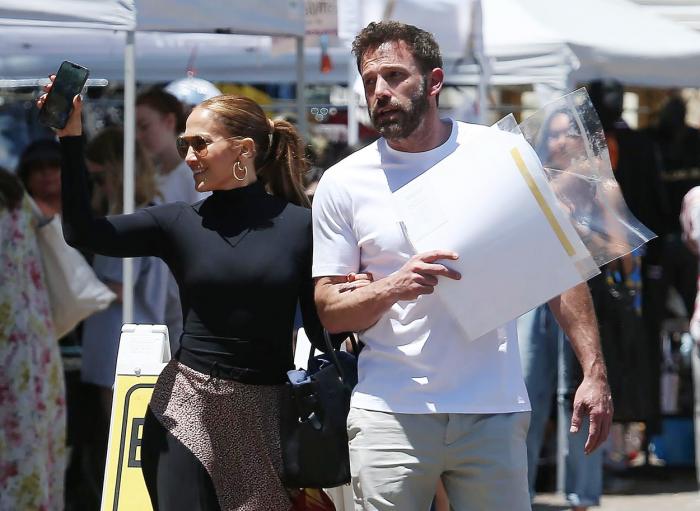 Jennifer Lopez poartă o bluză neagră și pantaloni animal print, iar Ben Affleck poartă un tricou alb și pantaloni deschiși la culoare