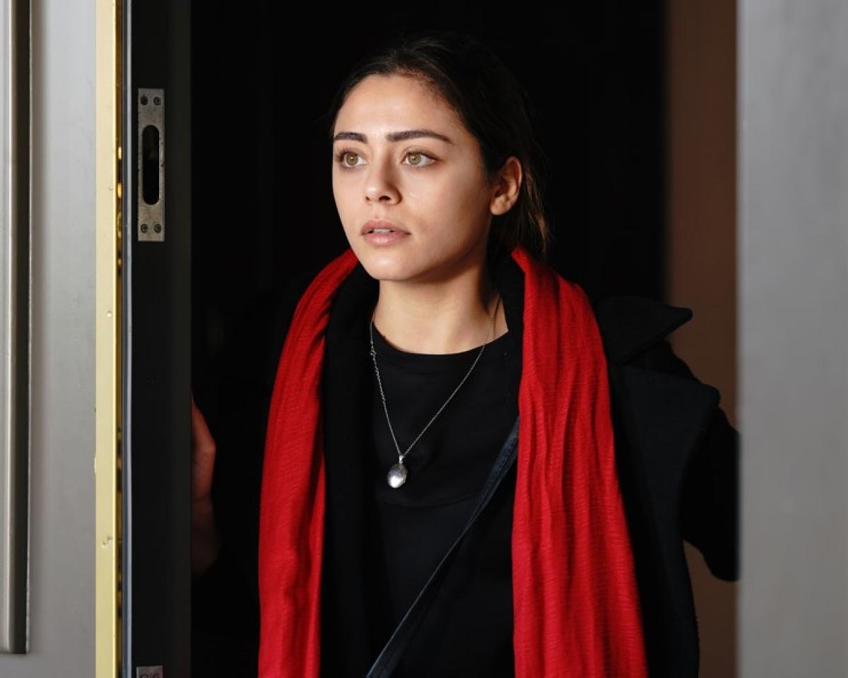 Sıla Türkoğlu poartă o haină neagră și un fular roșu