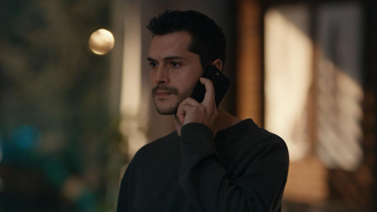 Alperen Duymaz poartă o bluză neagră cu mâneci lungi și ține telefonul la ureche cu mâna stângă