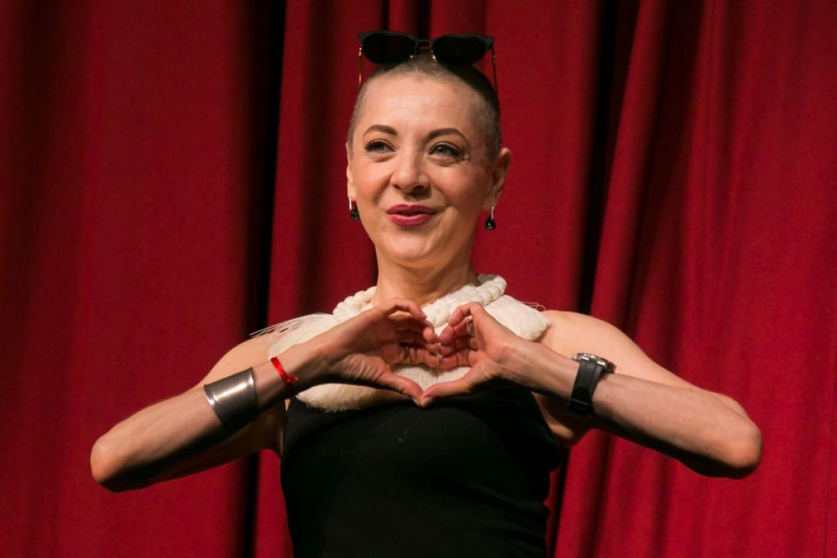 Edith González poartă o rochie fără mâneci și își ține mâinile împreunate în formă de inimă