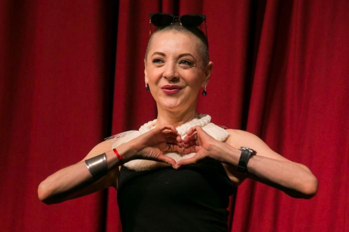 Edith González poartă o rochie fără mâneci și își ține mâinile împreunate în formă de inimă