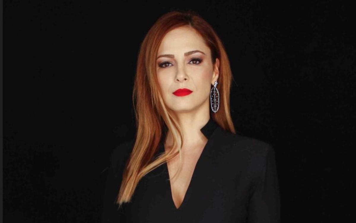 Mine Tugay poartă un costum negru și are părul desprins și ruj roșu pe buze