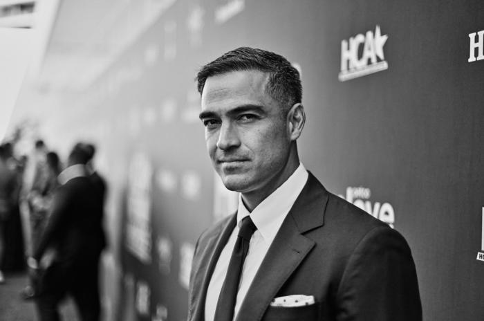 Alfonso Herrera poartă un costum închis la culoare, însă fotografia este alb-negru. Se află pe covorul roșu