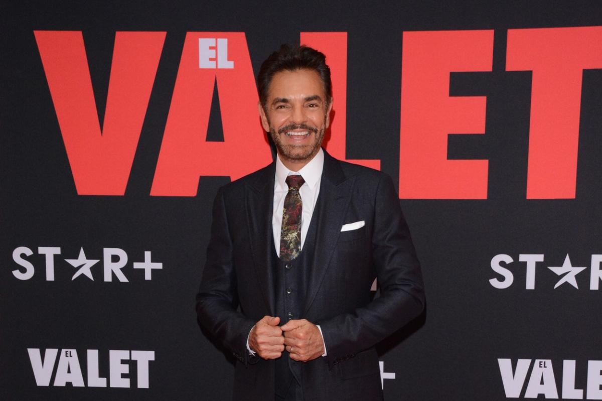Eugenio Derbez poartă un costum negru și cămașă albă. Actorul zâmbește