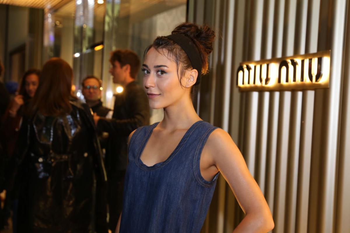 Merve Çağıran poartă o bluză albastră fără mâneci și își ține mâna stângă în șold. Actrița poartă părul prins