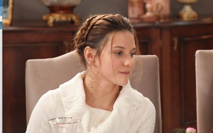 Alina Boz poartă o bluză albă cu mâneci lungi și are părul prins într-un coc împletit