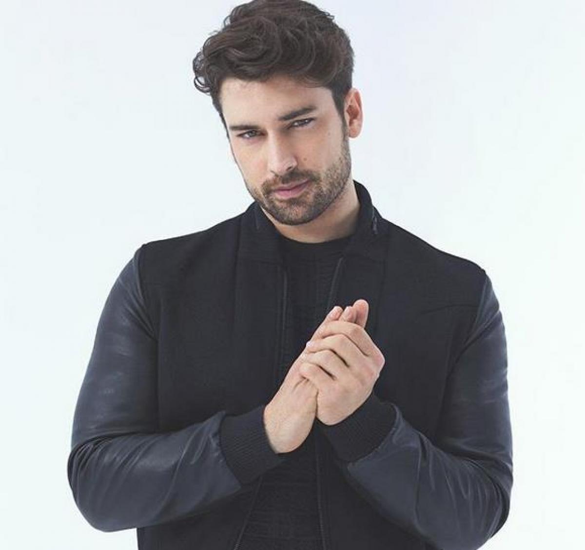 Alp Navruz poartă o geacă neagră de piele și își ține mâinile împreunate