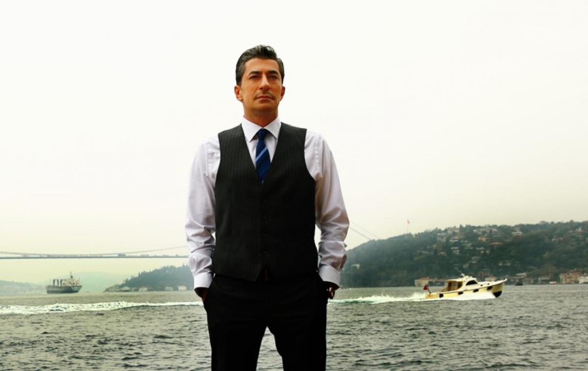 Erkan Petekkaya poartă o cămașă albă, ține mâinile în buzunar și are un sacou negru