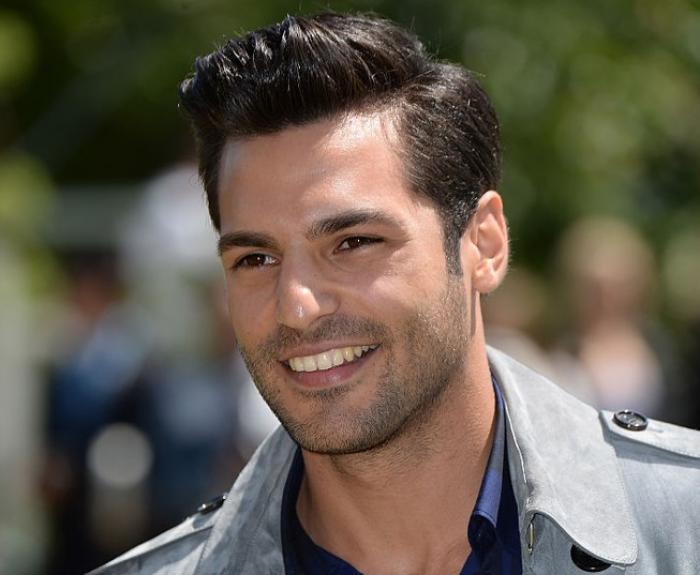 Serkan Çayoğlu poartă o cămașă și o geacă gri