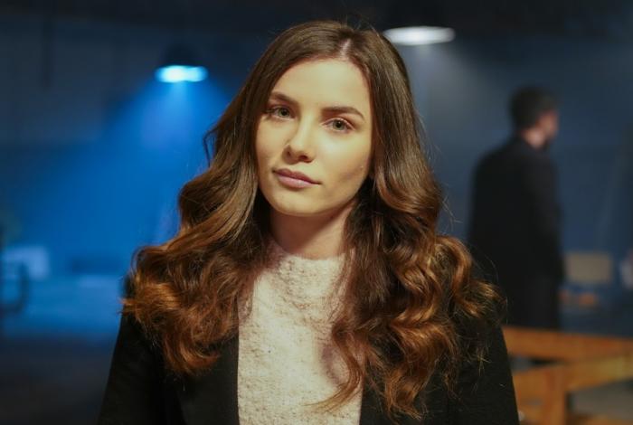 Cansu Tuman poartă o maletă pe gât, are părul desprins și ondulat
