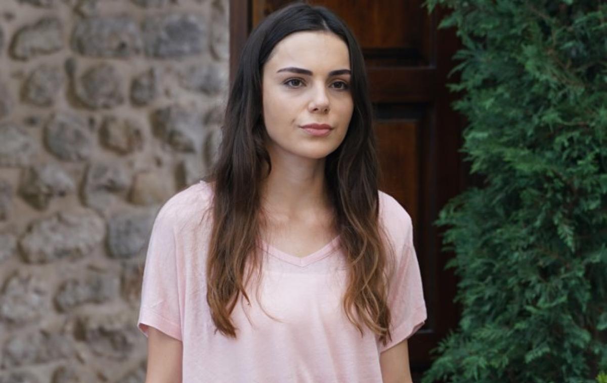 Yagmur Tanrisevsin poartă un tricou roz cu mâneci scurte și are părul lung, desprins