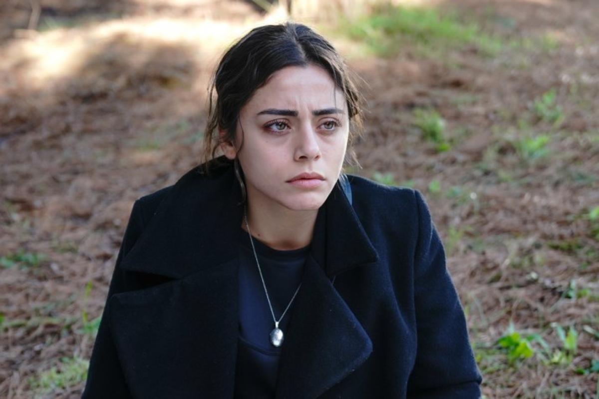 Sıla Türkoğlu poartă o bluză neagră și un palton de acceași culoare și stă pe jos