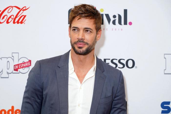 William Levy poartă o cămașă albă și un sacou de culoare gri. Actorul se află pe covorul roșu în cadrul unui eveniment important