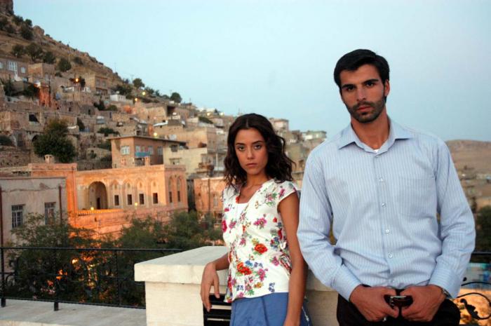 Mehmet Akif Alakurt poartă o cămașă deschisă la culoare și își ține mâinile în dreptul curelei