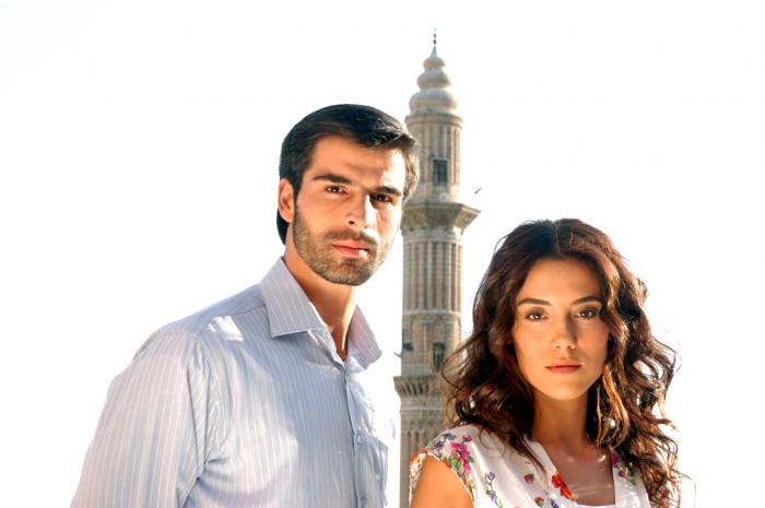 Mehmet Akif Alakurt poartă o cămașă deschisă la culoare și stă alături de colega Cansu Dere