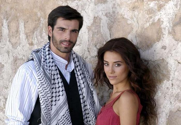 Mehmet Akif Alakur poartă o cămașă albă, un sacou negru și o eșarfă