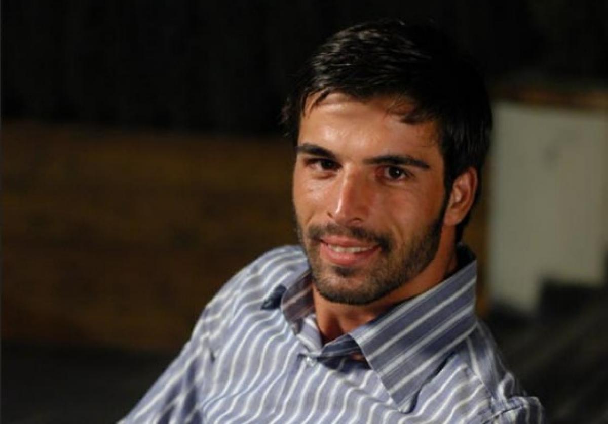 Mehmet Akif Alakur poartă o cămașă albastră cu dungi și zâmbește