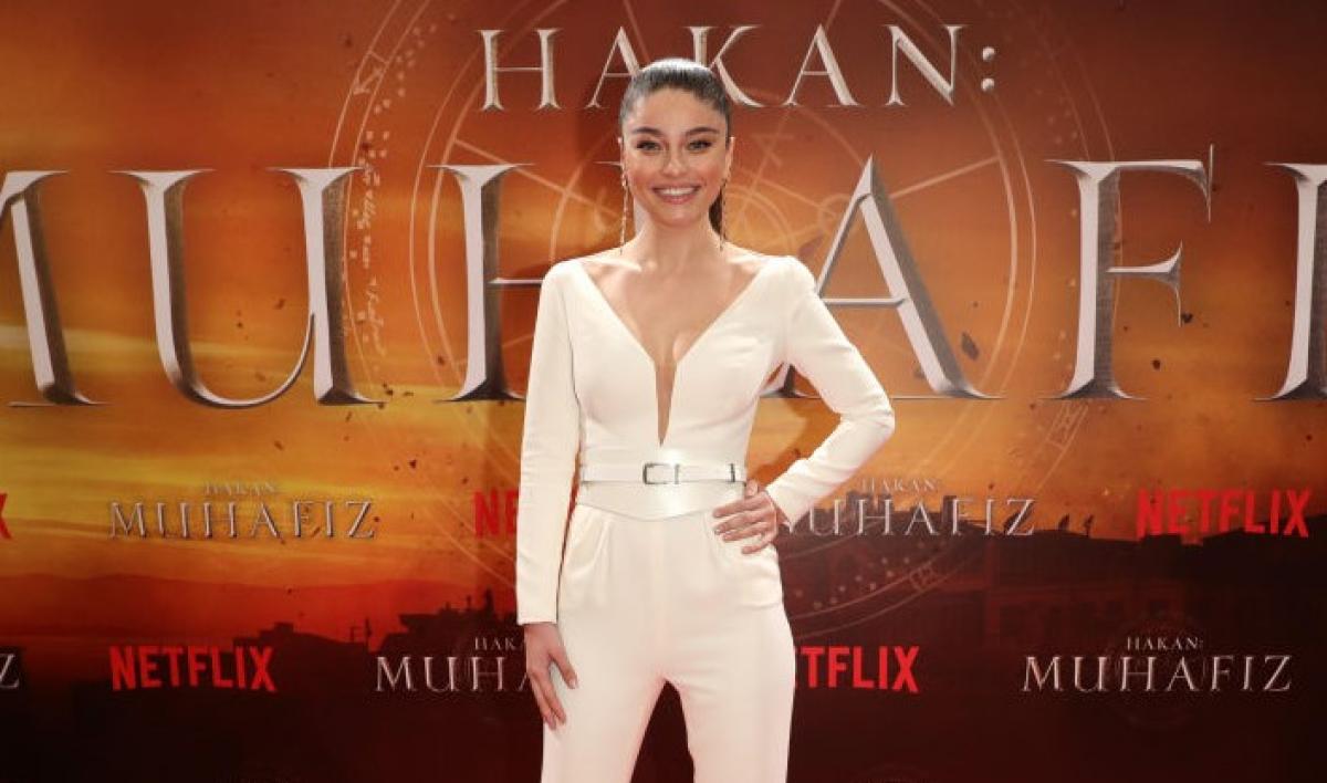 Ayça Ayşin Turan poartă un costum alb cu mâneci lungi și cu decolteu