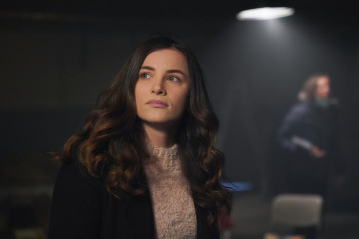 Cansu Tuman poartă o maletă de culoare maro deschis, are părul lung și desprins, ondulat și se uită într-o parte