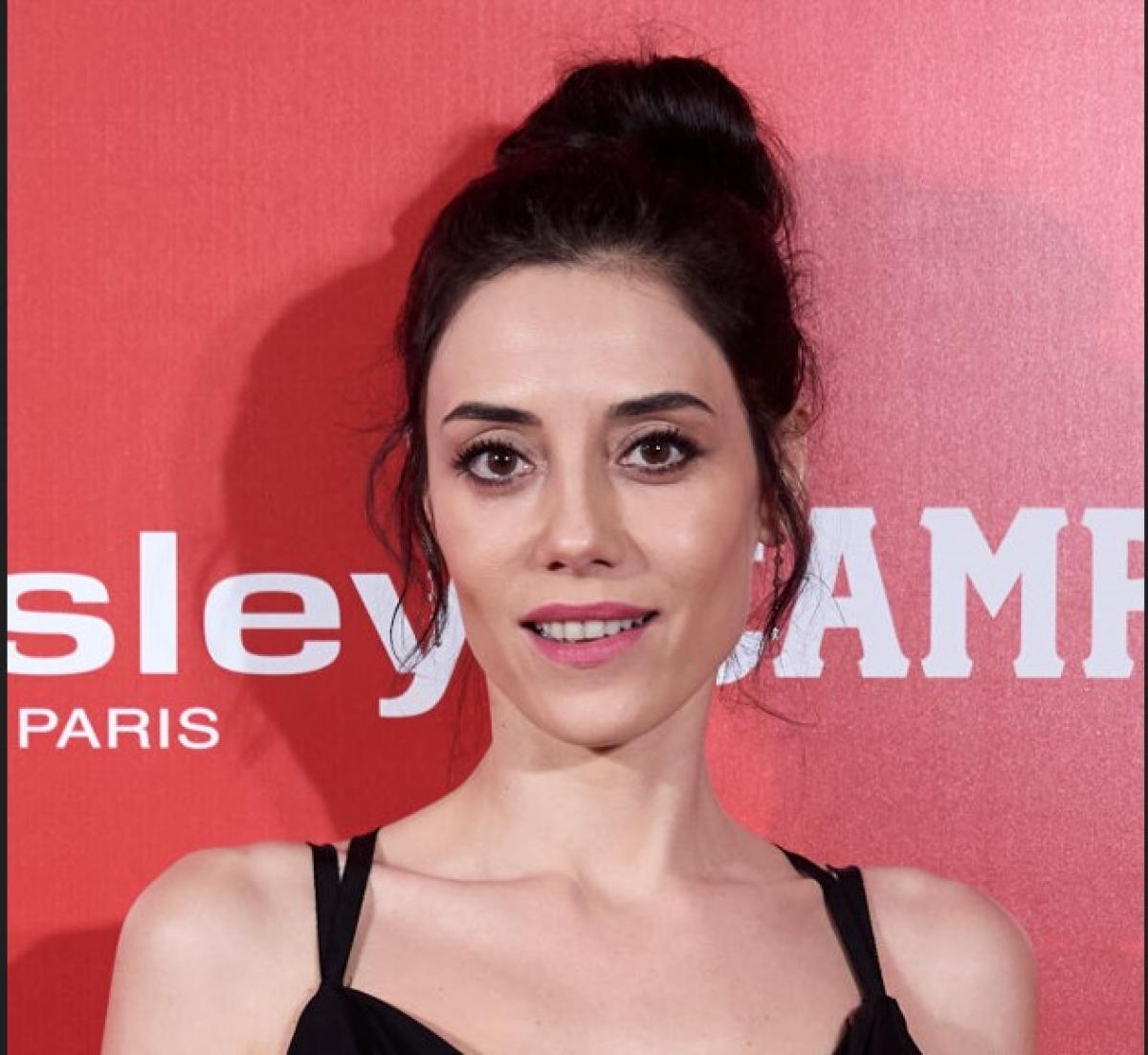 Cansu Dere poartă o rochie neagră fără mâneci și are părul prins în coc