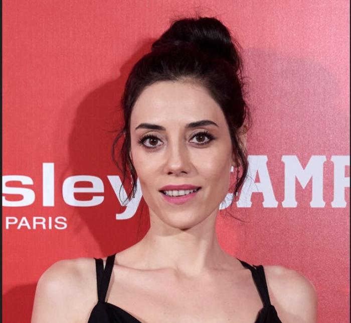 Cansu Dere poartă o rochie neagră fără mâneci și are părul prins în coc