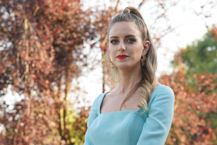 Bige Önal poartă o rochie albastră cu mâneci lungi și are părul prins pe jumătate