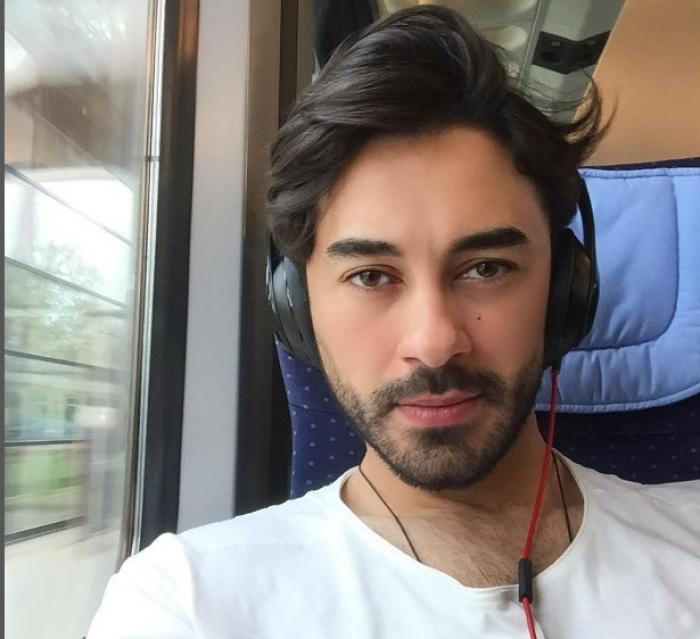 Gokhan Alkan poartă un tricou alb și își ține căștile la urechi