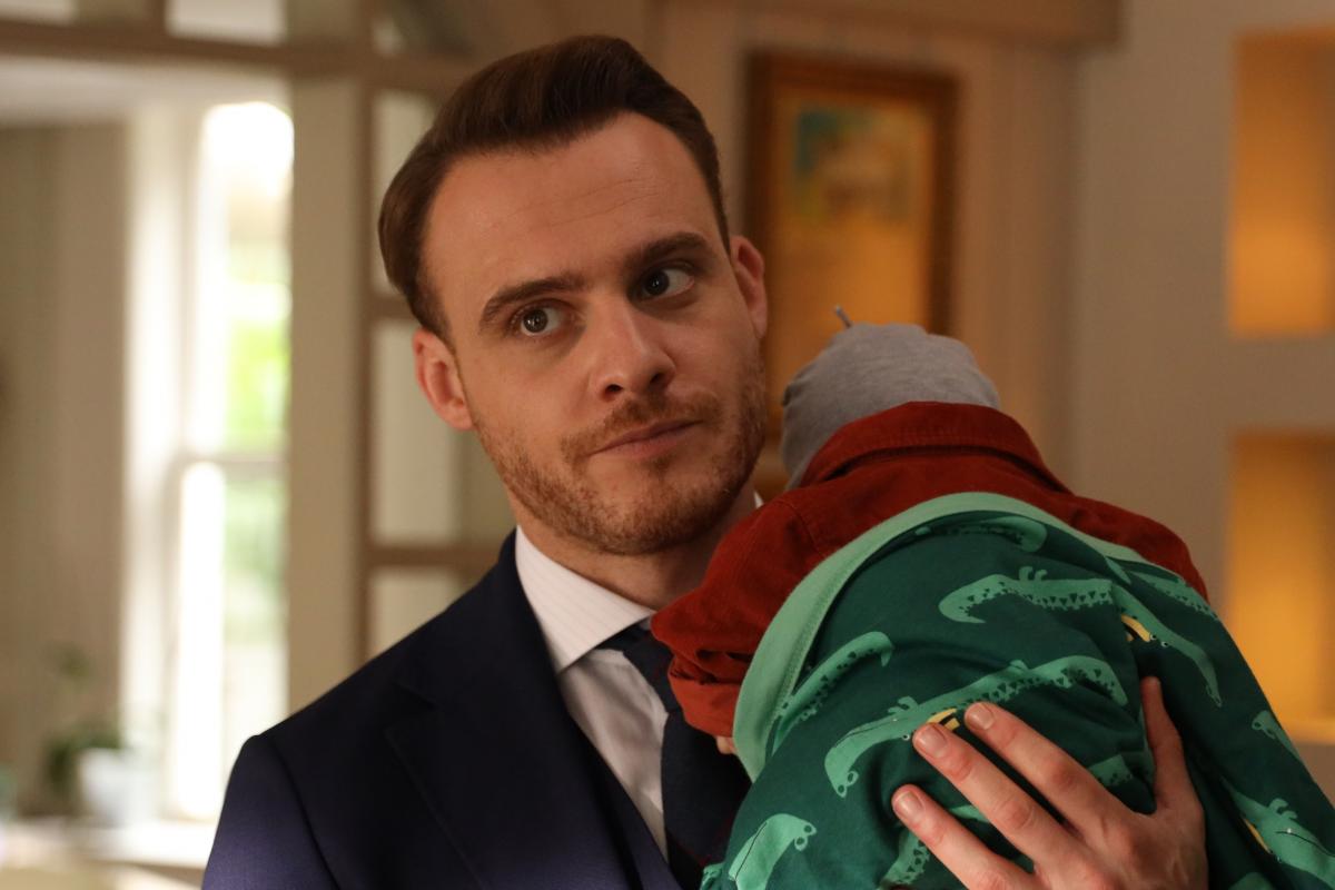 Kerem Bursin poartă o cămașă albă și ține un bebeluș în brațe
