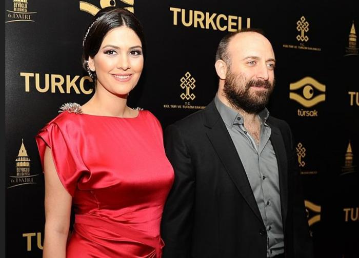 Bergüzar Korel poartă o rochie roșie, zâmbește și are părul prins. Stă lângă Halit Ergenc ce poartă o cămașă gri și un sacou negru