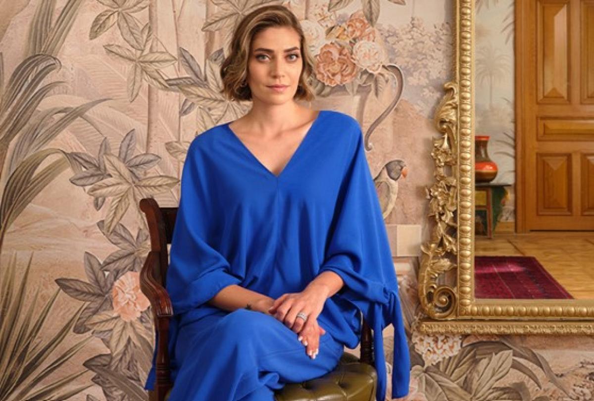 Öznur Serçeler poartă un costum albastru și stă pe scaun