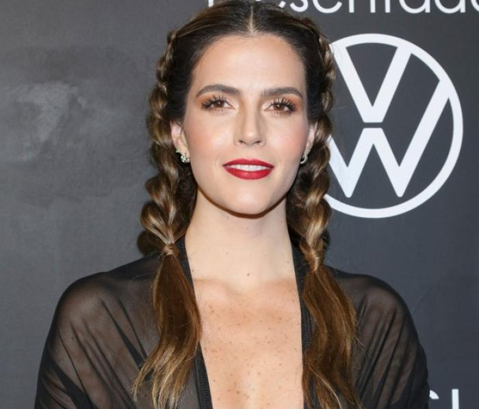 Claudia Álvarez poartă o bluză neagră cu decolteu și are cozi împletite