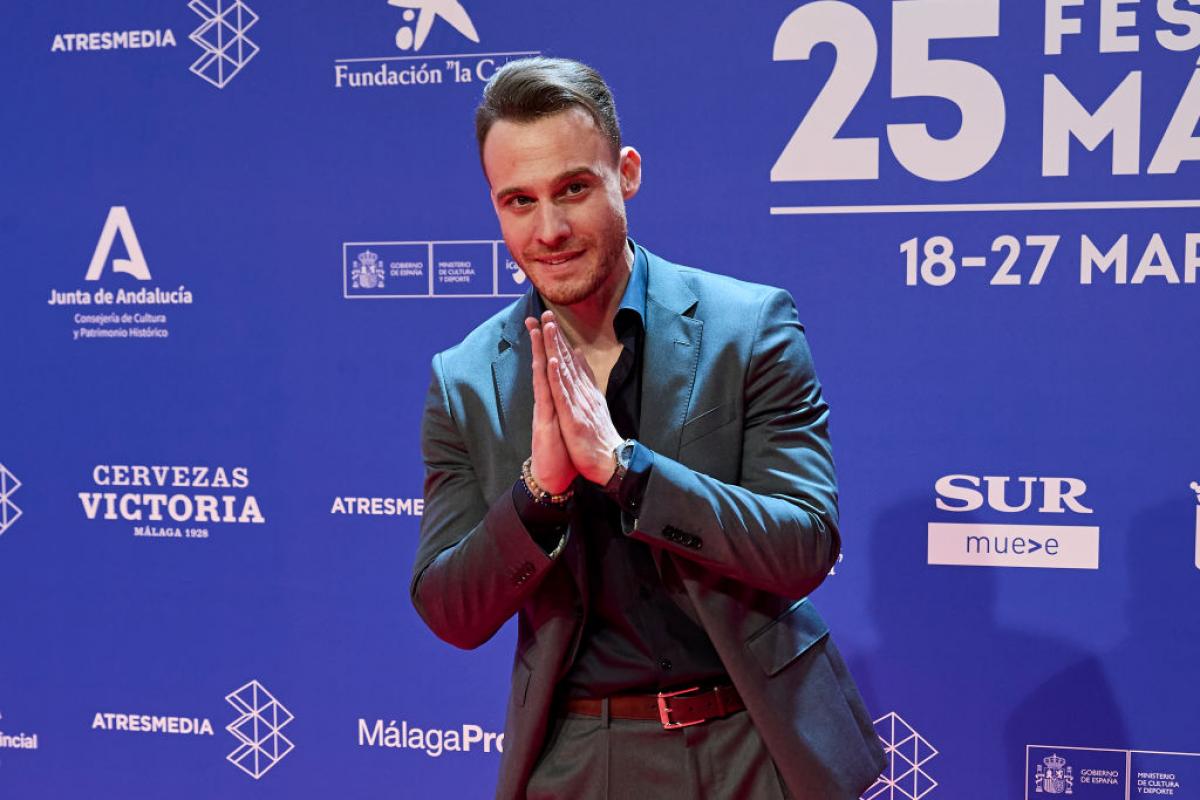 Kerem Bürsin poartă costum și își ține mâinile împreunate