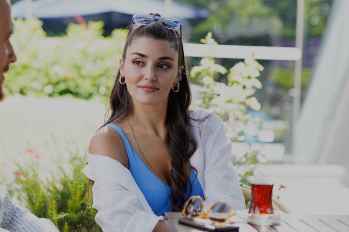 Hande Erçel poartă o bluză albă și zâmbește