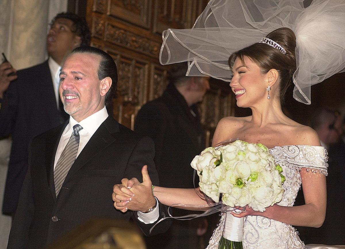 Thalia poartă o rochie albă de mireasă și îl ține de mână pe Tommy Mottola care poartă un costum negru și o cămașă albă și cravată