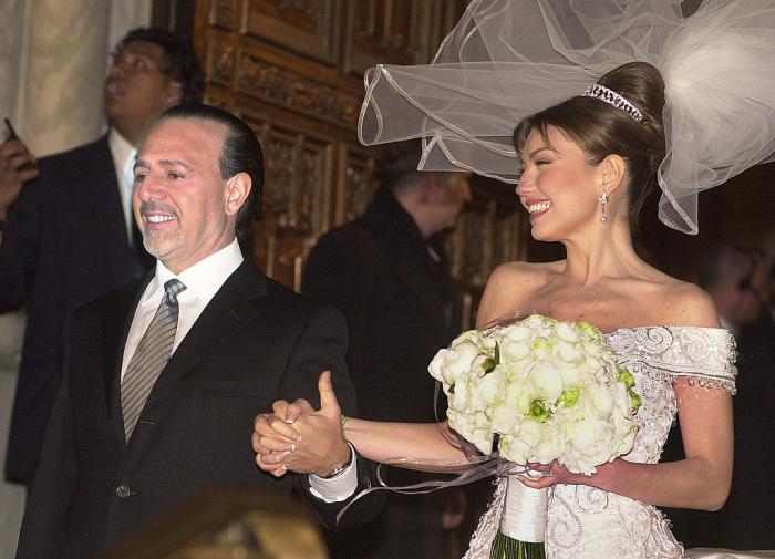 Thalia poartă o rochie albă de mireasă și îl ține de mână pe Tommy Mottola care poartă un costum negru și o cămașă albă și cravată