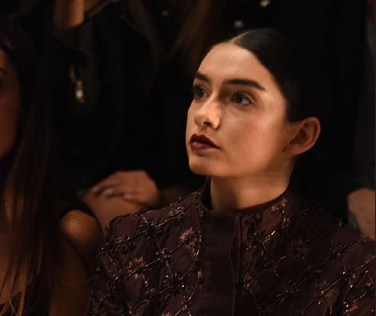 Hazar Ergüçlü poartă o rochie închisă la culoare, ruj închis și părul prins pe un fundal întunecat