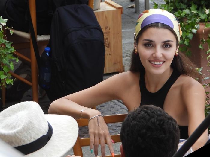 Hande Erçel poartă un maiou negru și o eșarfă colorată pe cap și zâmbește