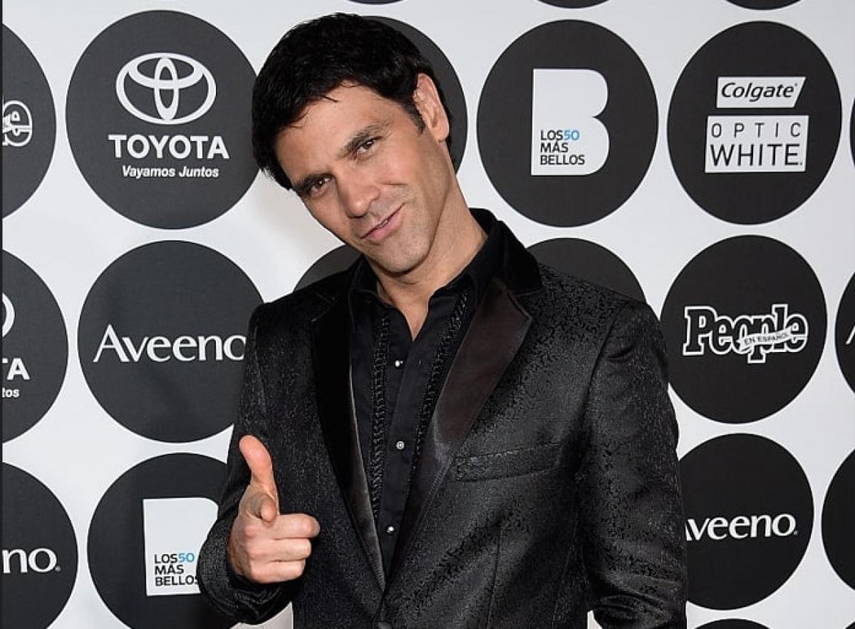 Valentino Lanús poartă o cămașă neagră și un sacou negru și zâmbește