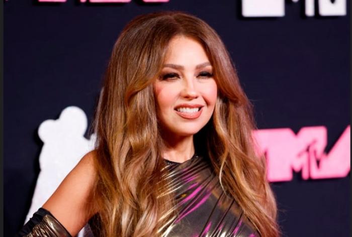 Thalía poartă o rochie lungă, părul desprins și zâmbește