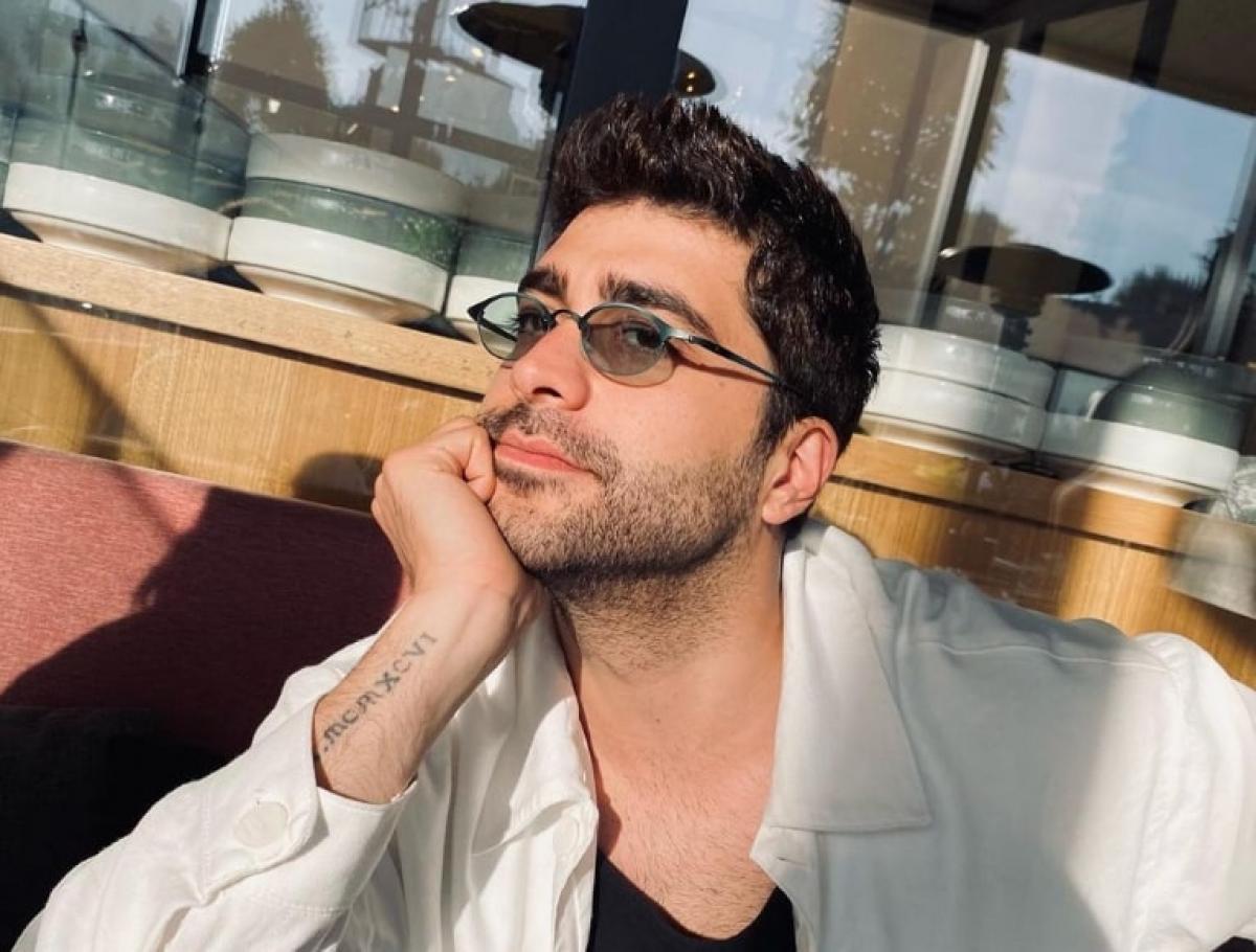 Doğukan Güngör poartă un tricou negru și o bluză albă cu mâneci lungi