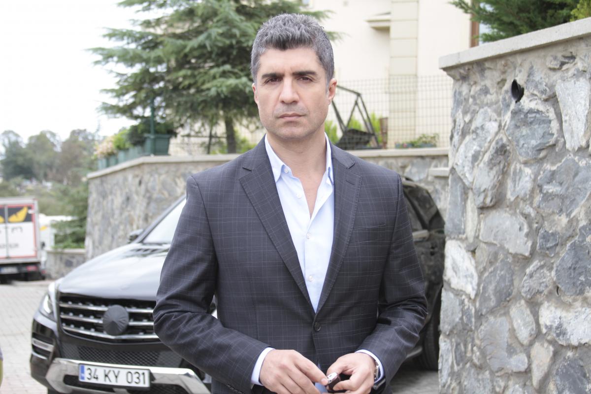 Özcan Deniz poartă o cămașă albă și un sacou gri