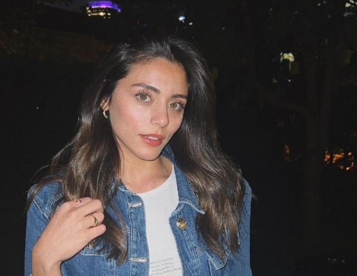 Sıla Türkoğlu poartă un tricou alb și o jachetă albastră cu părul lung desprins