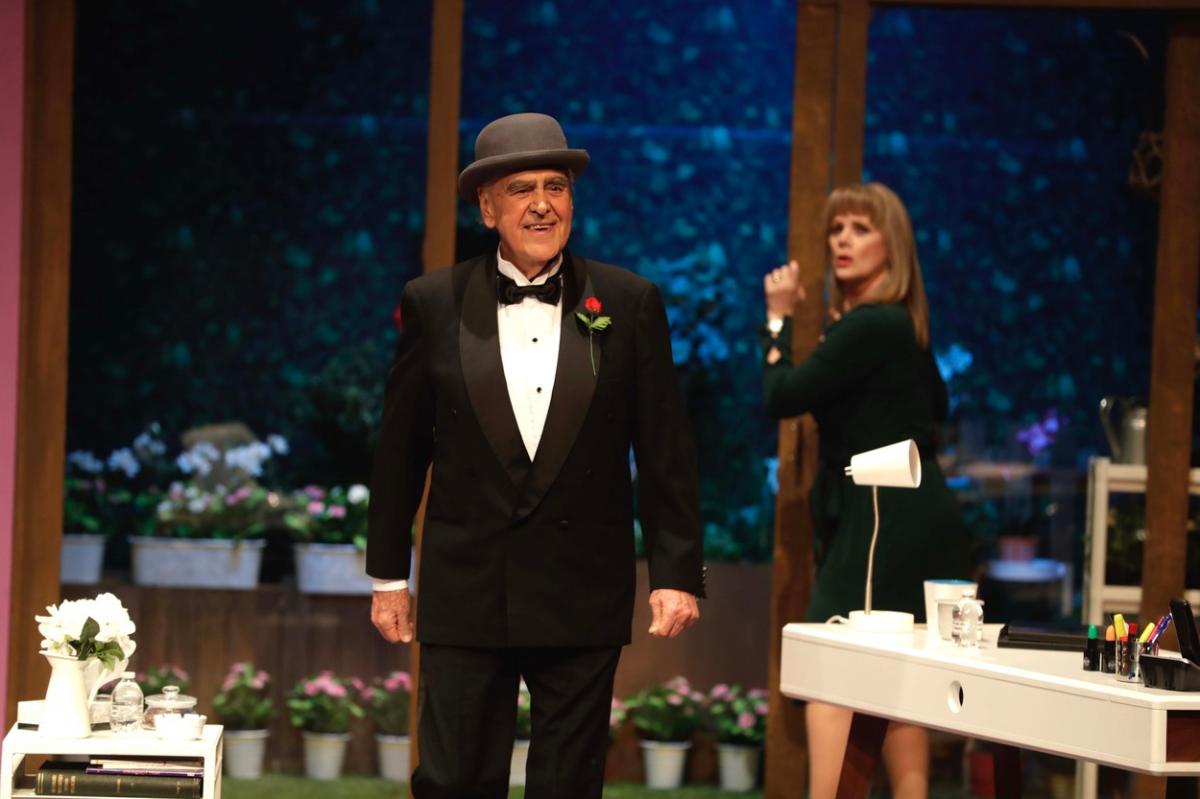 Eric del Castillo poartă un costum negru, cămașă albă și zâmbește