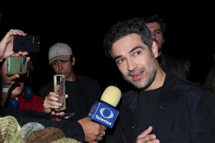 Alfonso Herrera poartă o bluză neagră cu mâneci lungi și vorbește la microfon
