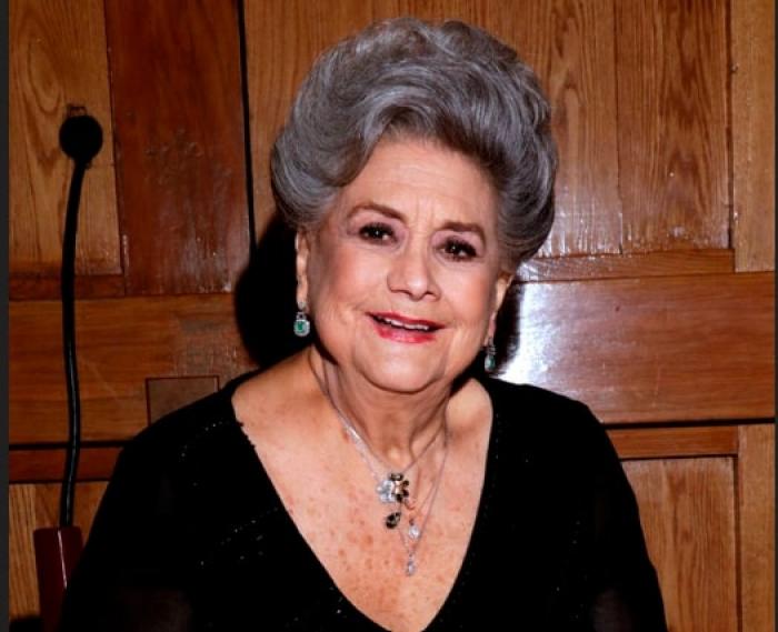 actriță poartă o rochie neagră cu mâneci lungi și zâmbește