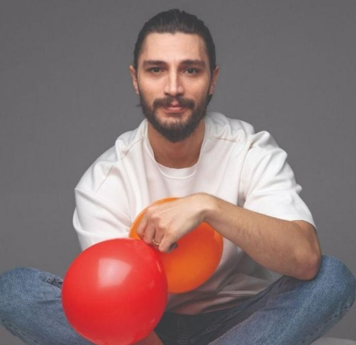 actor poartă o bluză albă cu mâneci lungi și blugi